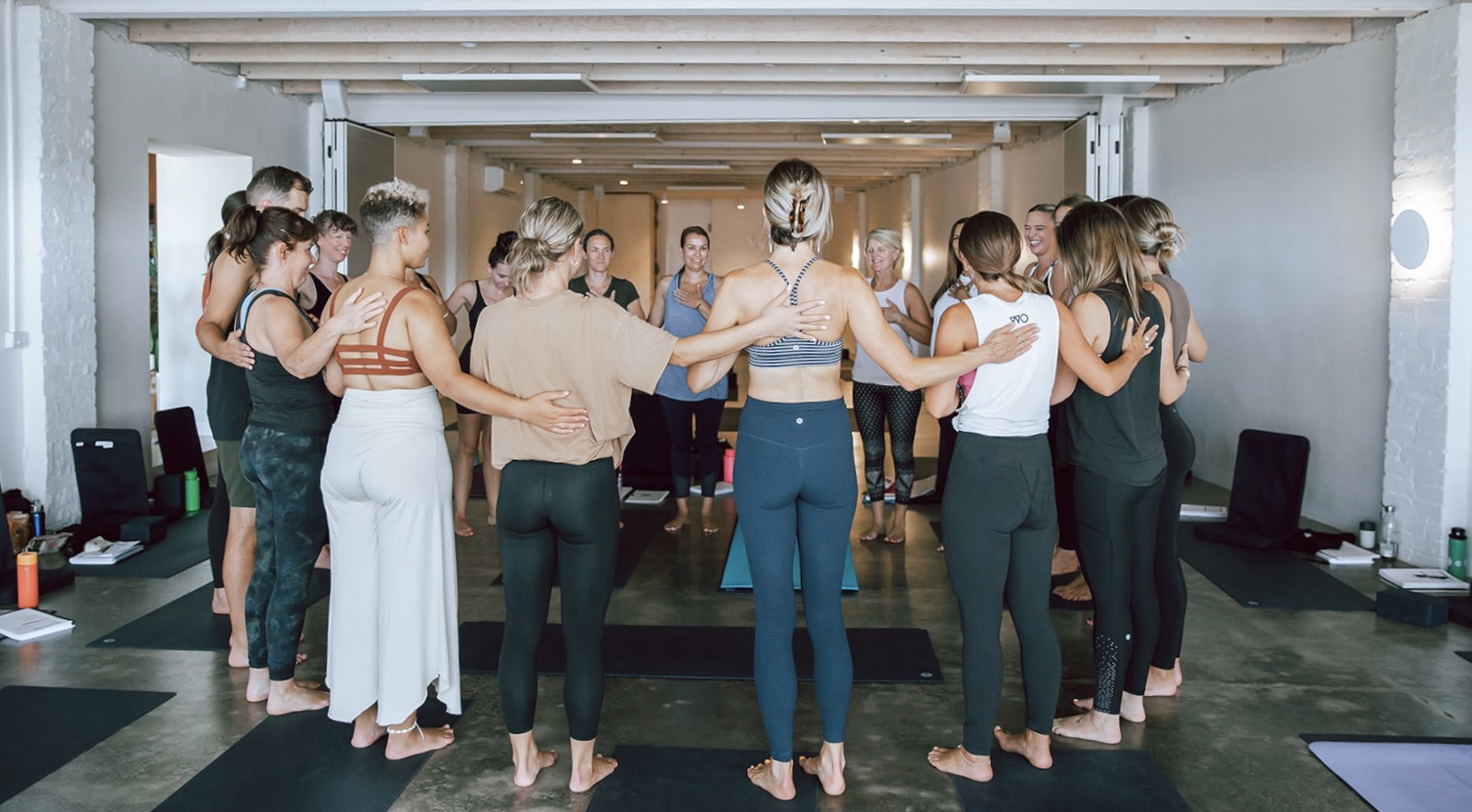 a group of students standing in a circle together with their arms around each other at warrior one yoga in mordialloc participating in a 200 hour vinyasa yoga teacher training